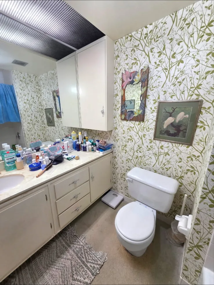 Dated wallpaper, cabinets and carpeted bathroom floor before work began